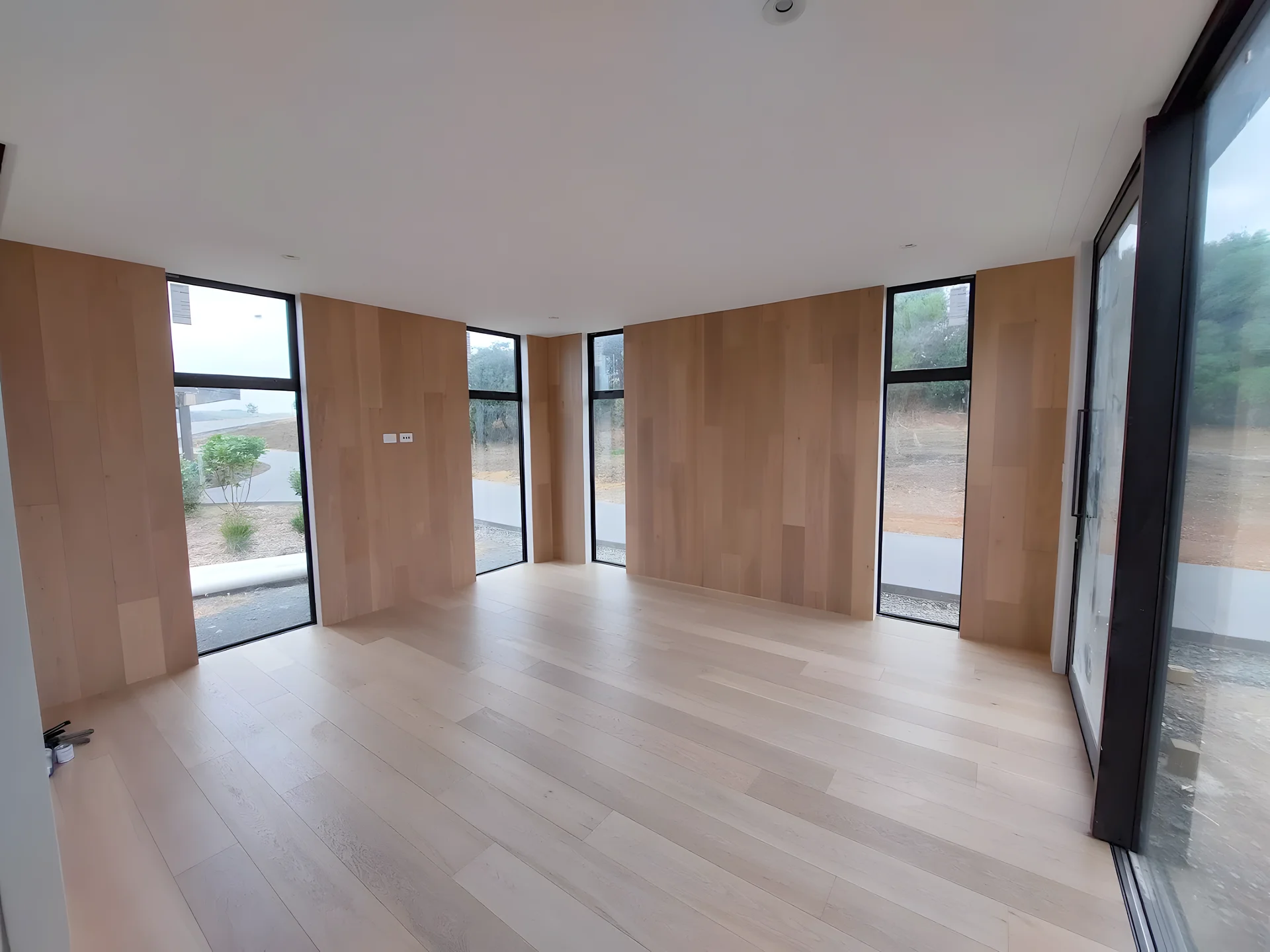 Wide-plank light oak floor in a room with timber-lined walls and tall windows