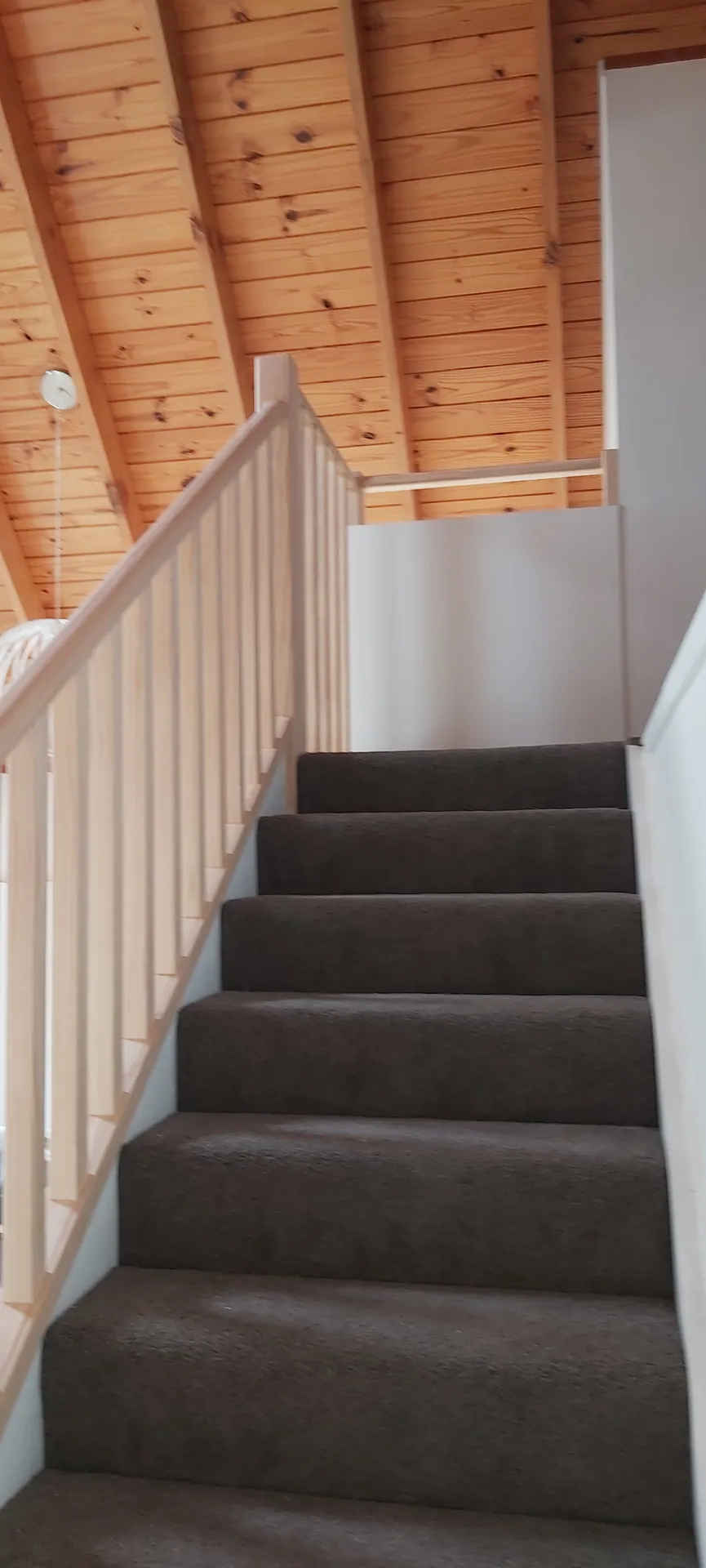 Carpeted staircase with a pine post and baluster balustrade under a timber-lined ceiling.