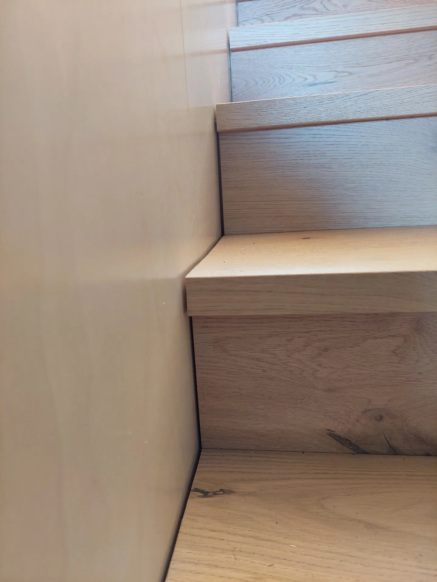 Close-up of oak stair treads and risers meeting a plywood wall.