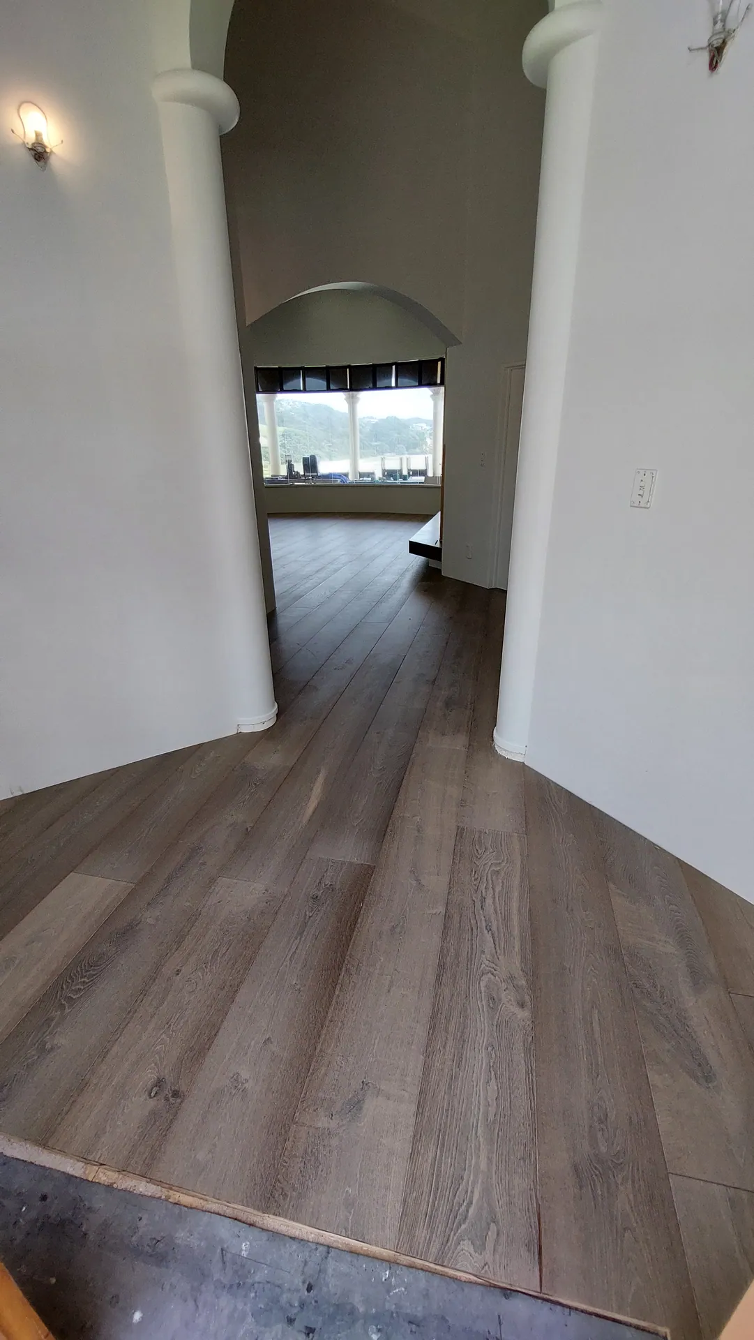 Grey-brown oak boards running between two round columns toward an arched opening, with an unfinished edge in front.