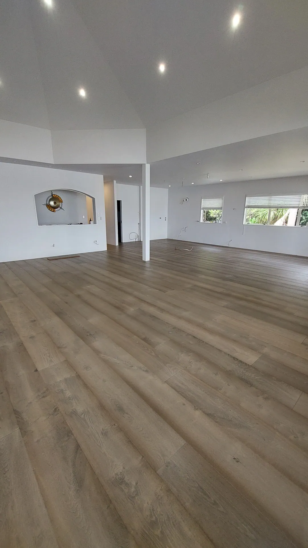 An empty open-plan room with a single column, arched niche and wide grey-brown oak boards.