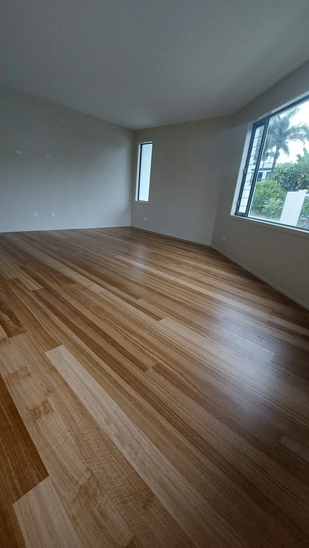 A glossy honey-toned strip timber floor in an empty room with a large window.