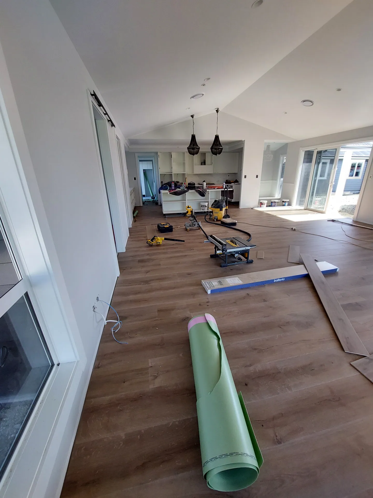 Floor being laid across an open-plan room with an underlay roll and saws on the floor.