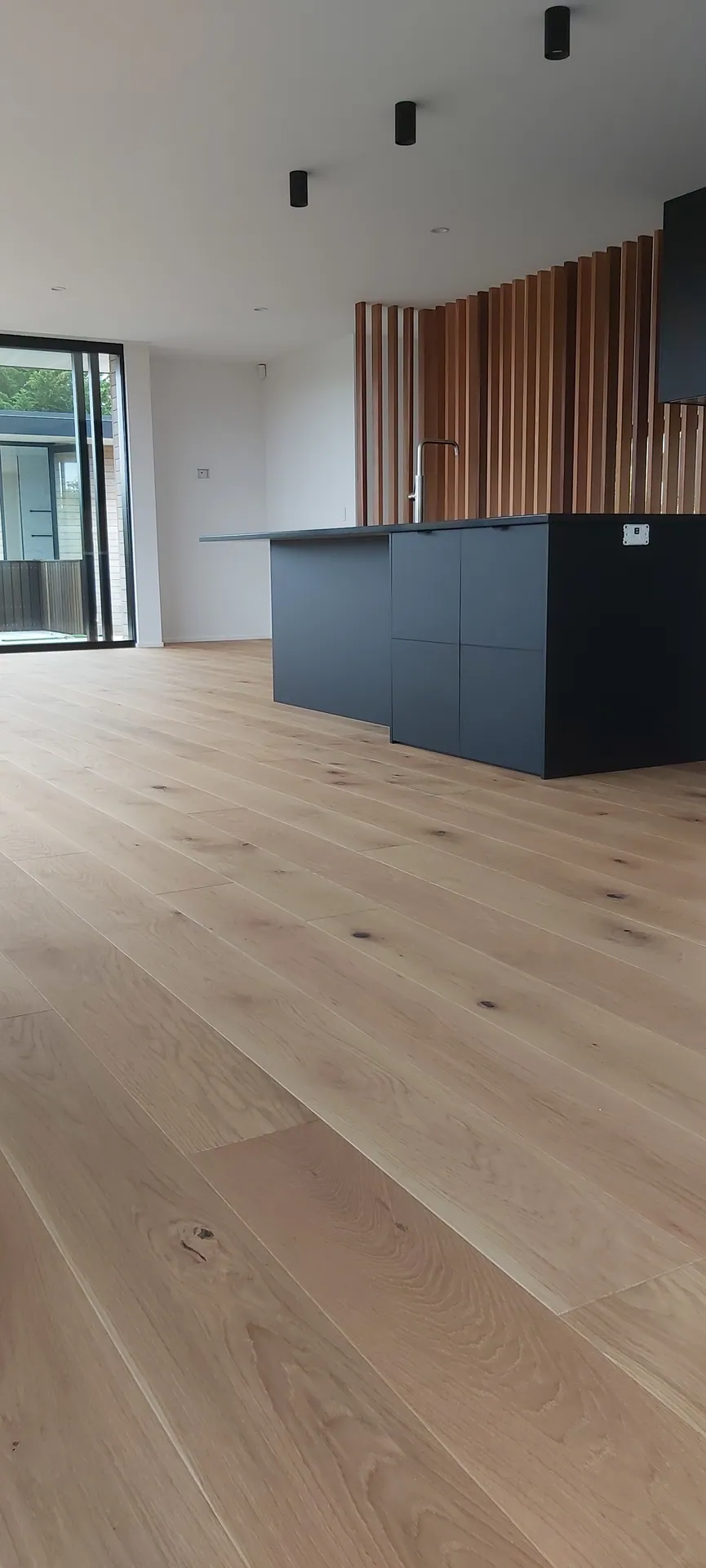 Light oak floor around a dark kitchen island.
