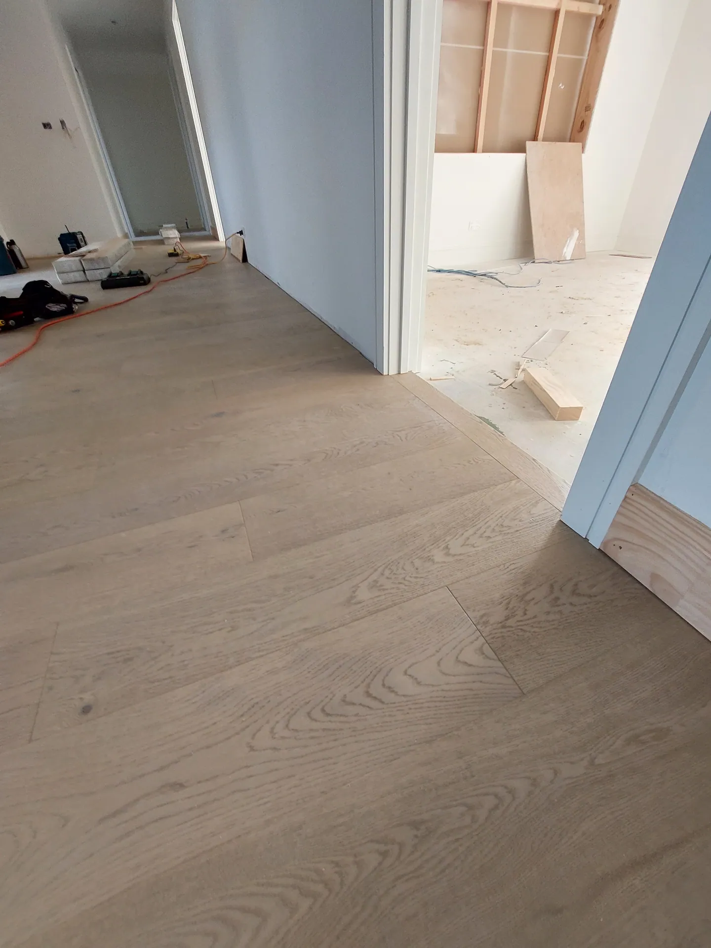 Light oak floorboards laid through a hallway and into a room still under construction.