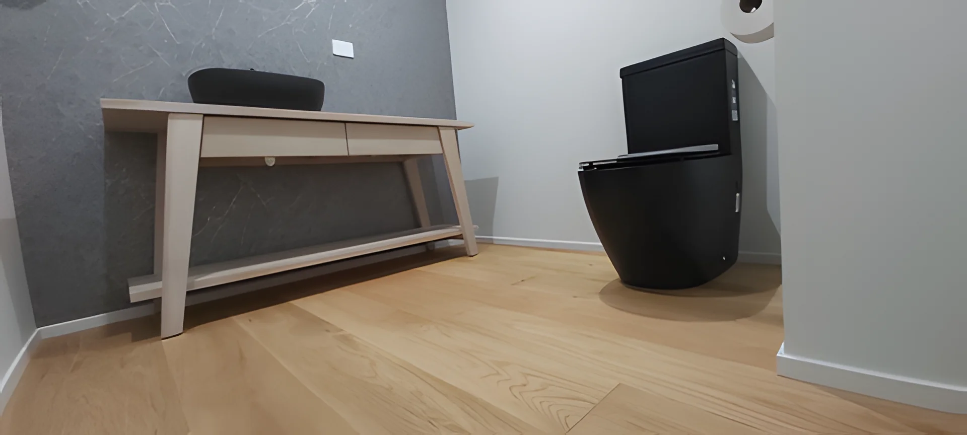 Low-angle view of a light timber floor in a small powder room with a timber vanity and a black toilet.