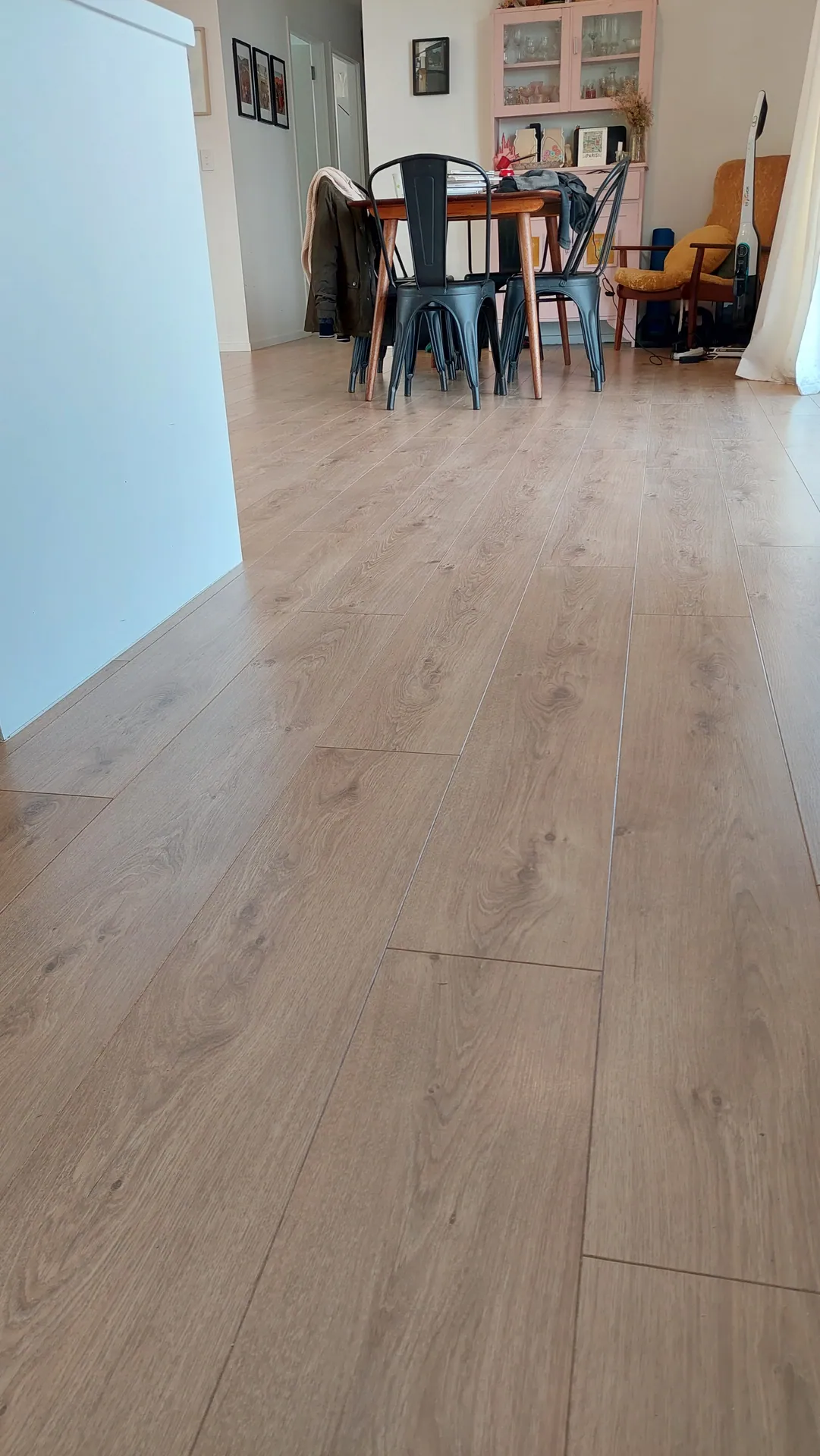 A light grey-brown plank floor running along a hallway into a lived-in dining area with a table and chairs.