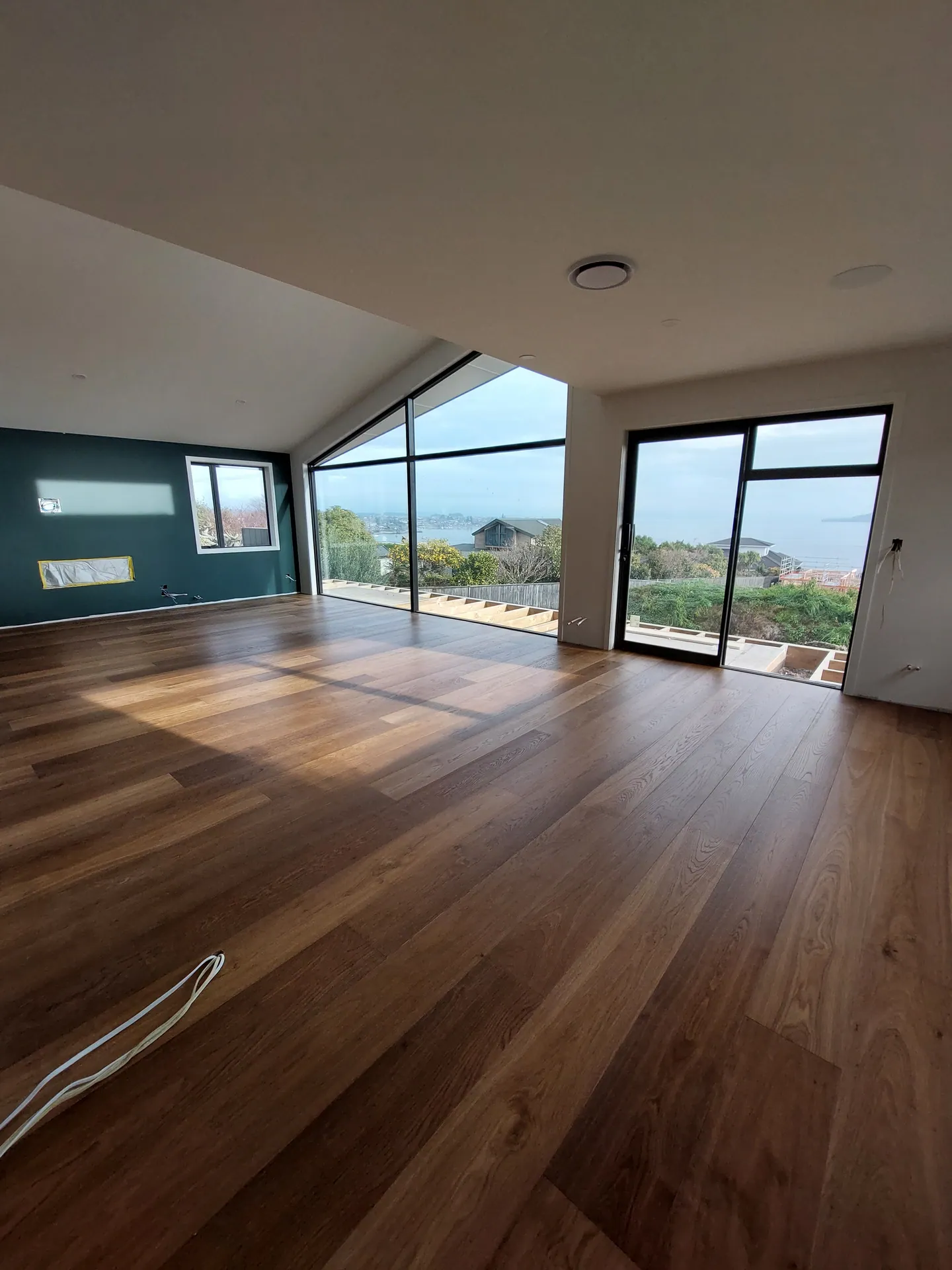 Large living room with dark timber floor, a raked glass wall and a view over the water.