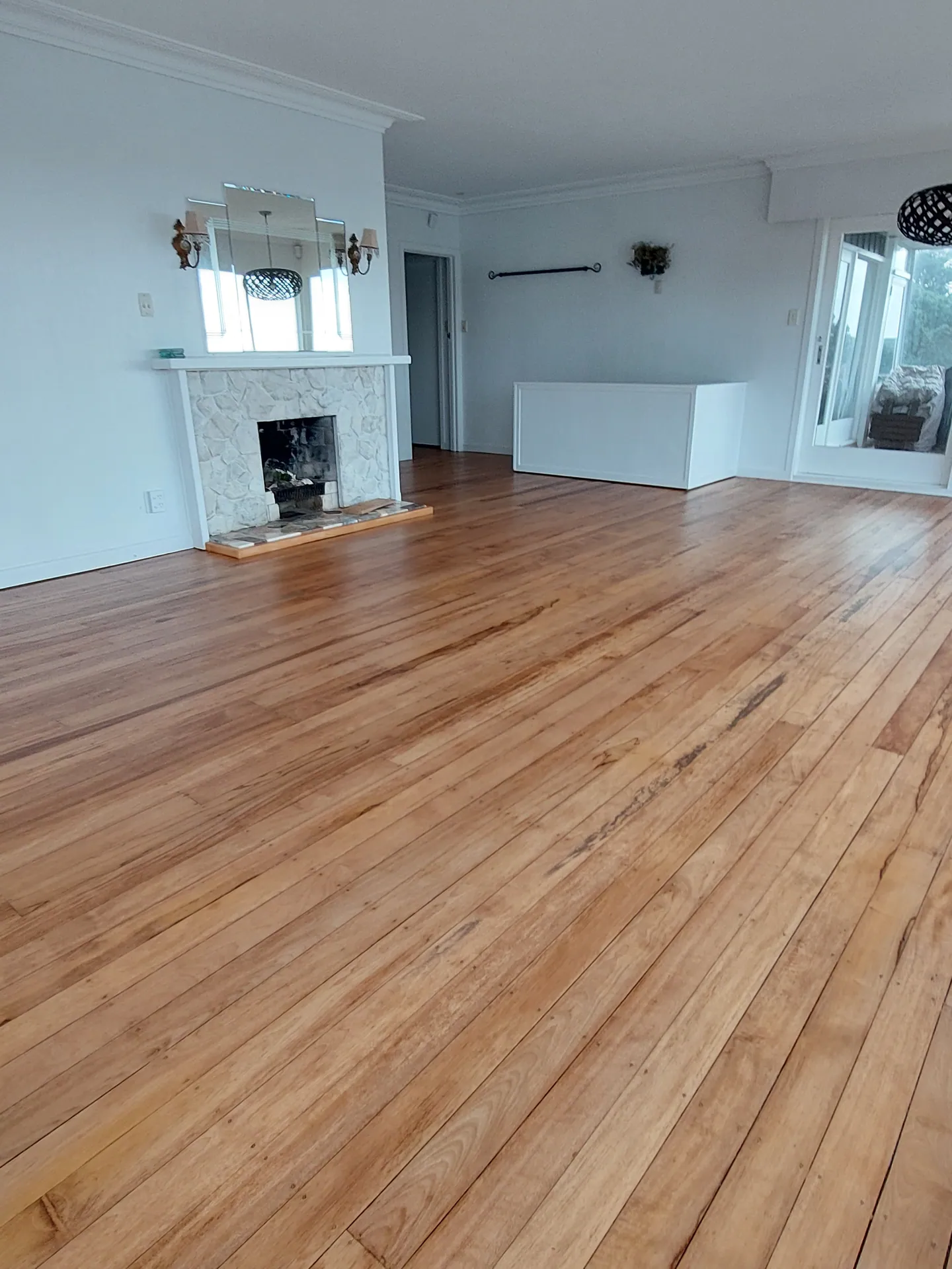 Refinished native timber floor in a white lounge with a tiled fireplace.