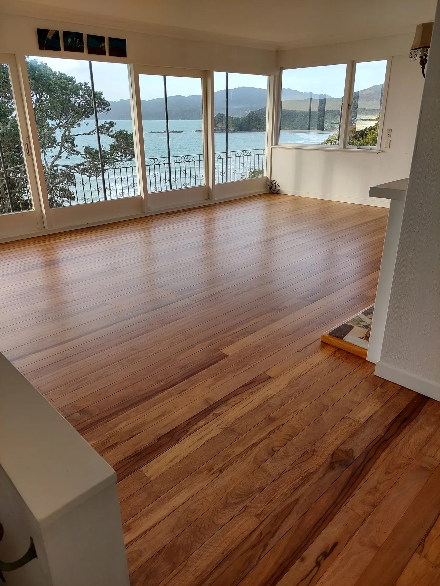 Refinished native timber floor in a lounge with a wall of windows looking over a bay and hills.