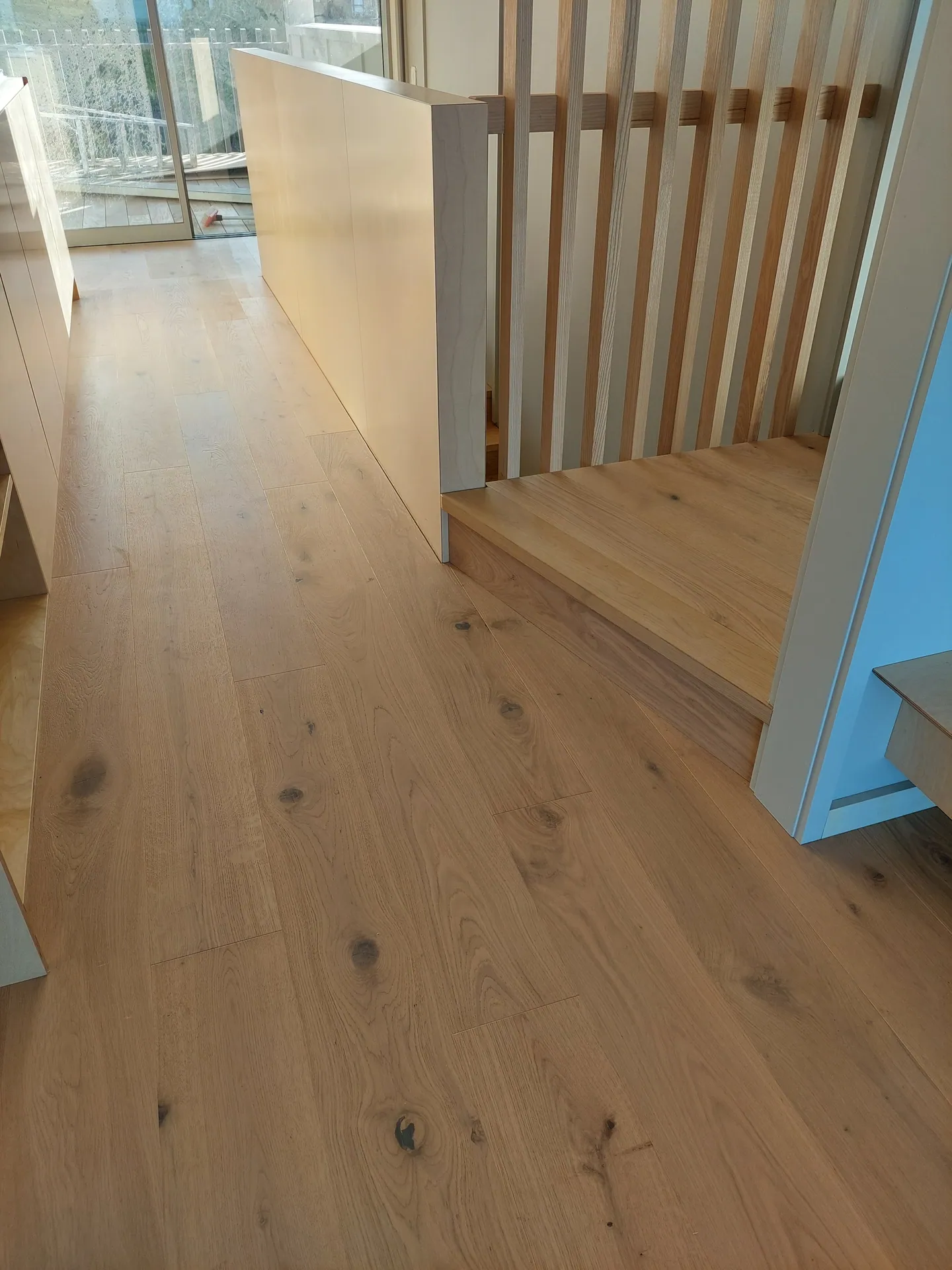 Wide oak floorboards with visible knots running past a slatted timber screen and stair opening.