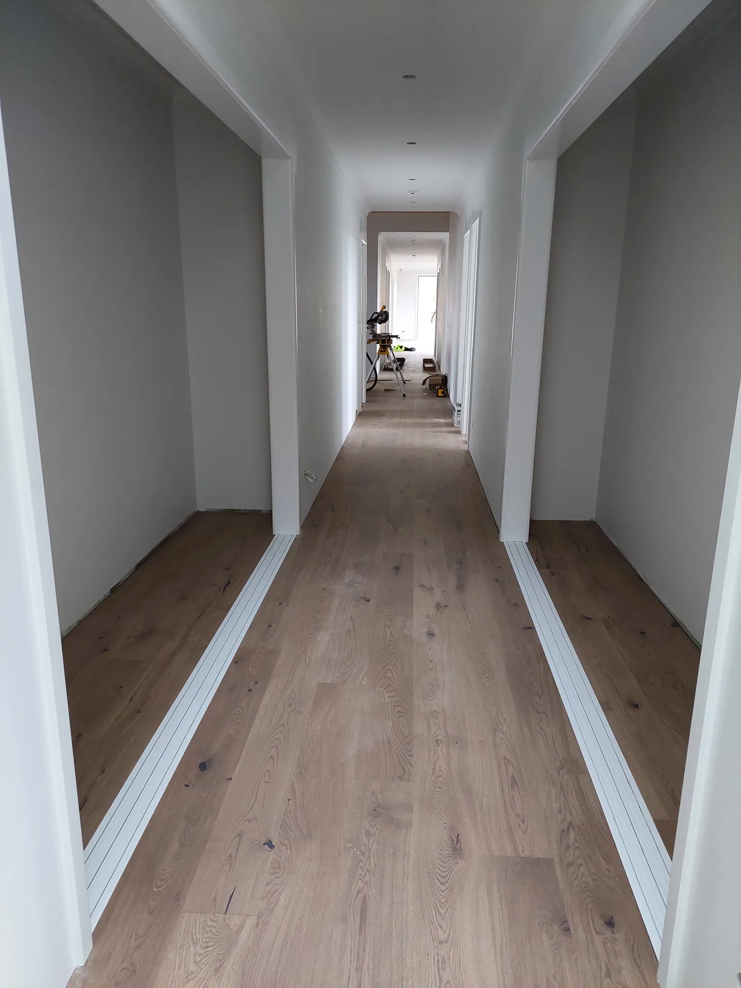 Long hallway with light oak floorboards and open doorways on both sides.