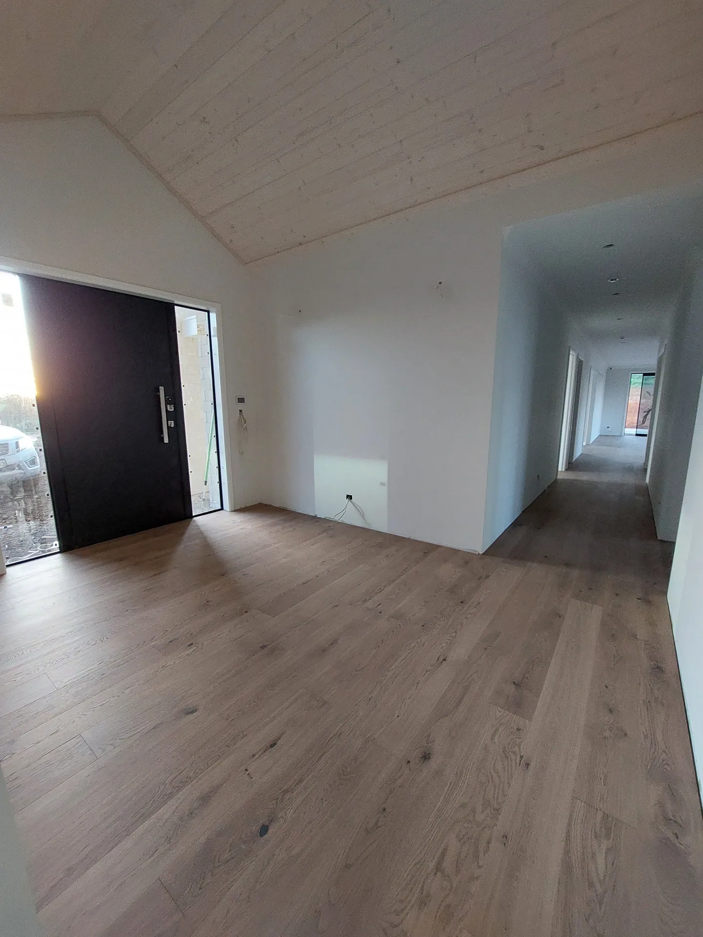 Entry with oak floorboards, a black front door and a hallway leading off under a timber-lined ceiling.