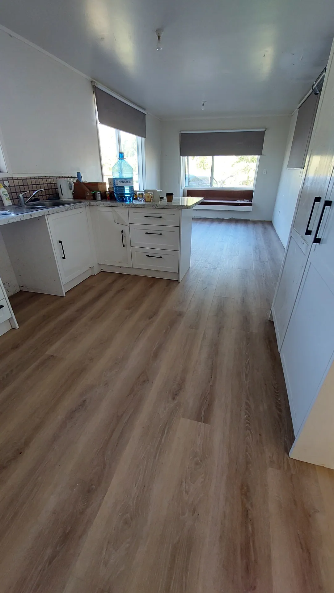 An oak-look plank floor running past white kitchen cabinets to a window seat.