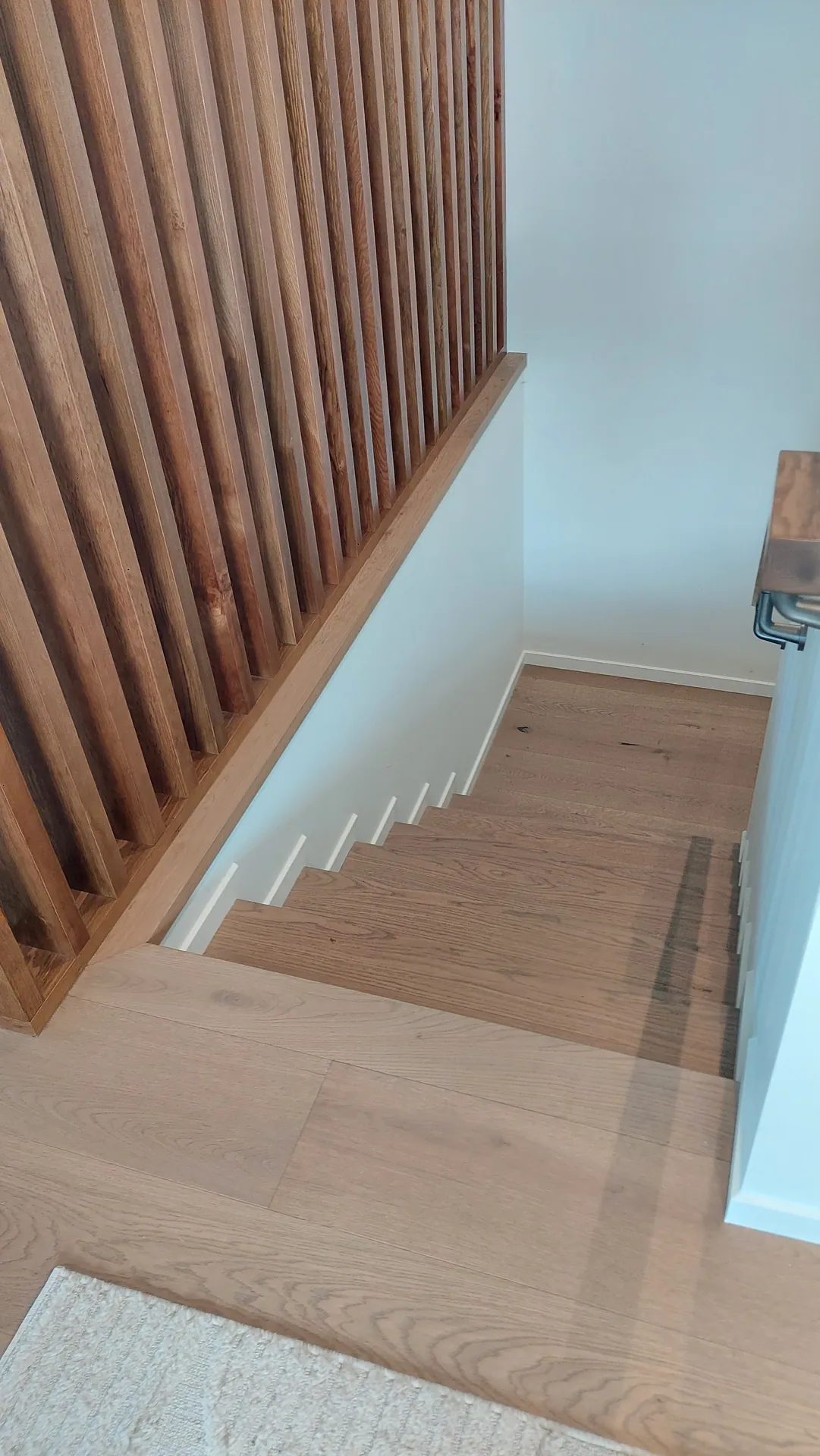 Looking down an oak staircase beside a vertical timber batten screen, from an oak-floored landing.