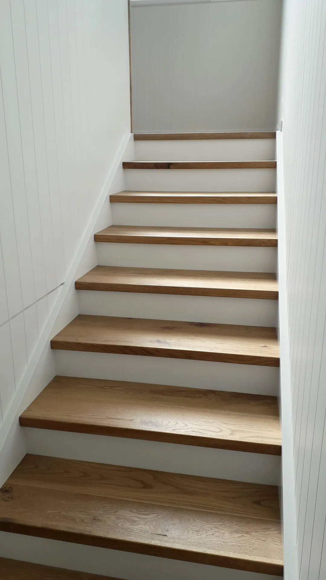 Oak treads with white risers up a narrow stair.