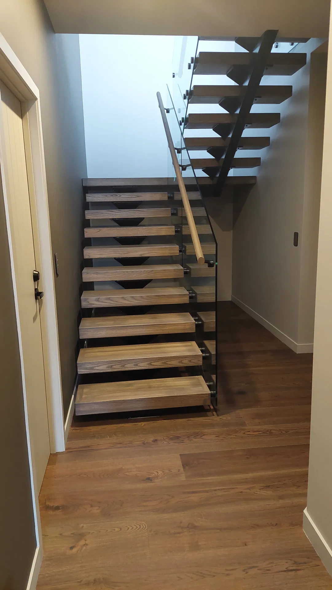 A floating staircase with thick oak treads, a glass balustrade and timber handrail, above a matching oak floor.