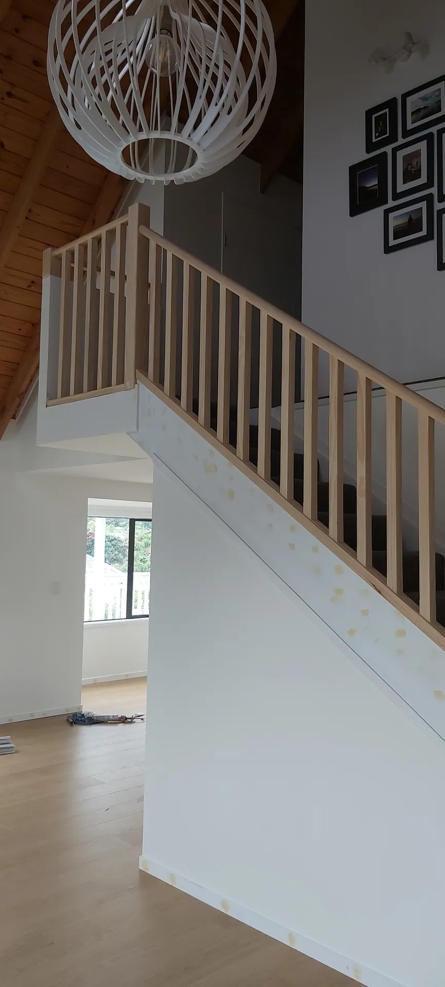 View from below of a pine balustrade running up a staircase and along the landing under a white pendant light.