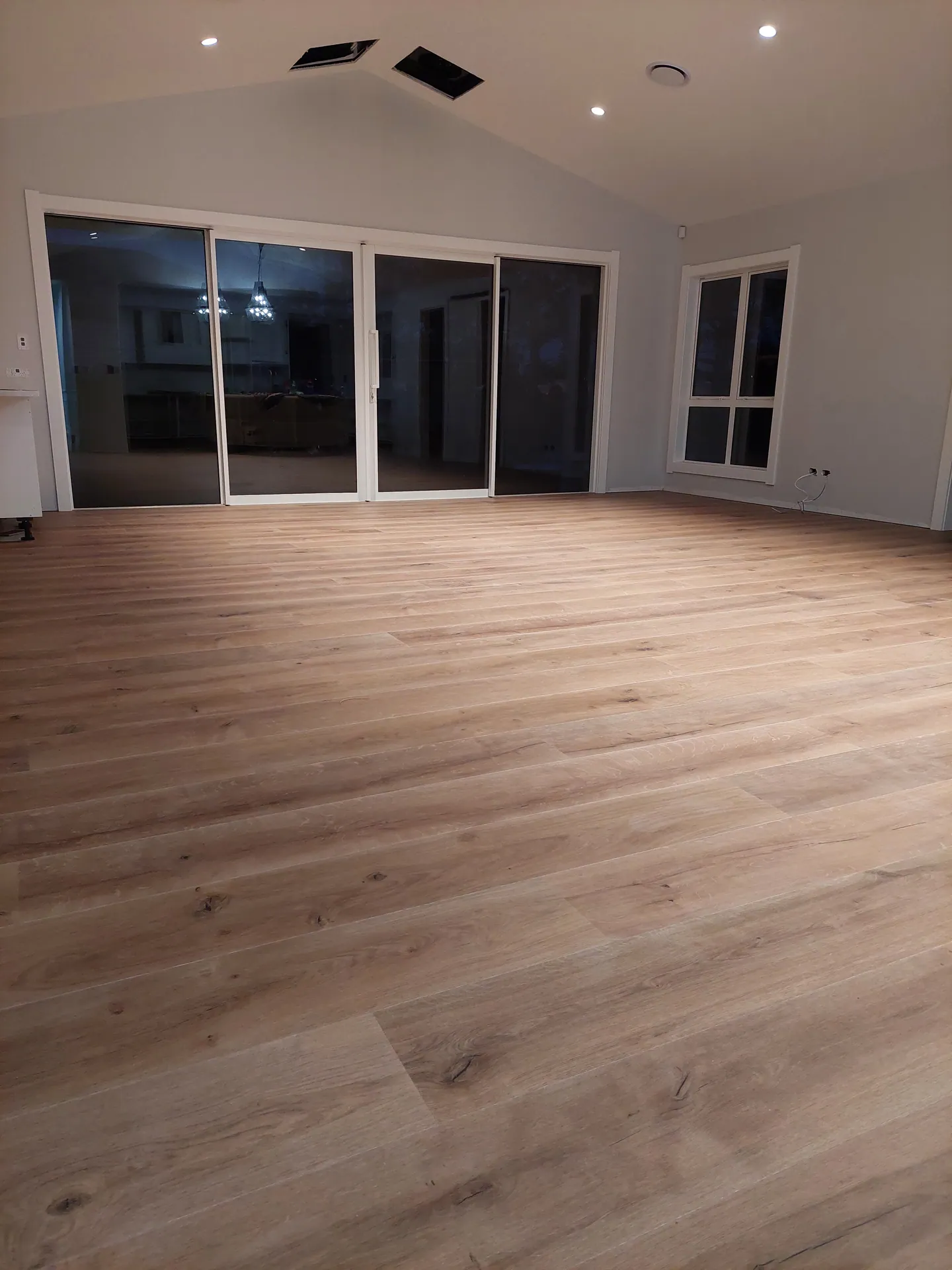 Large living room with a timber-look floor running to sliding glass doors under a raked ceiling.