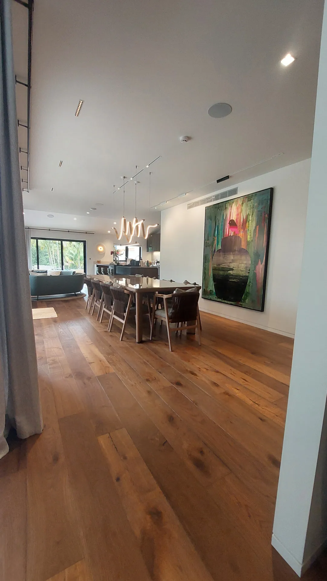 Wide brown oak boards running under a long dining table with a large painting on the wall.